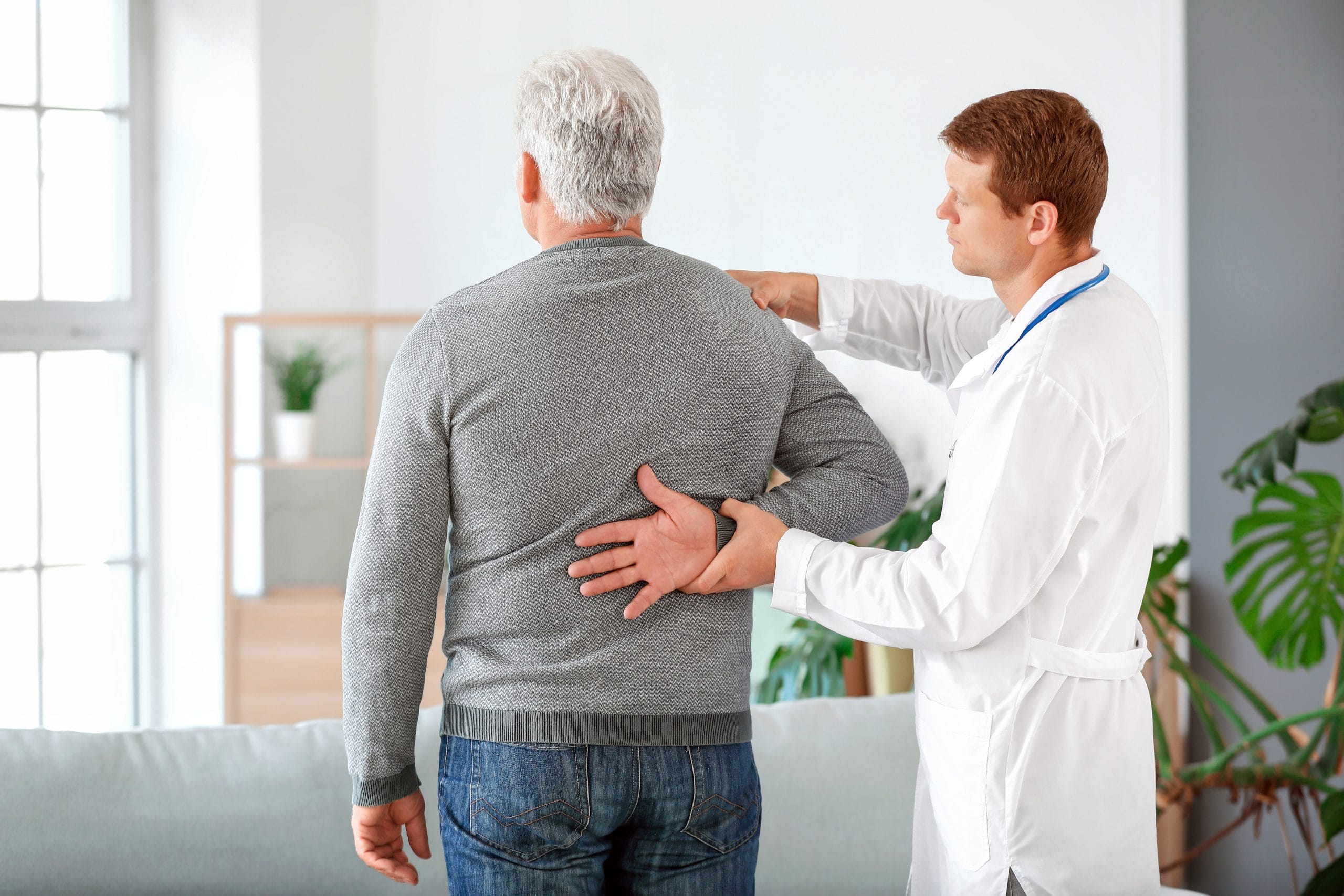 Doctor examining mature man with joint pain at home